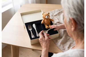 Grand-maman tenant la petite cuillère d’un set de couverts enfant Berndorf Carino, la main d’un bébé posée dessus